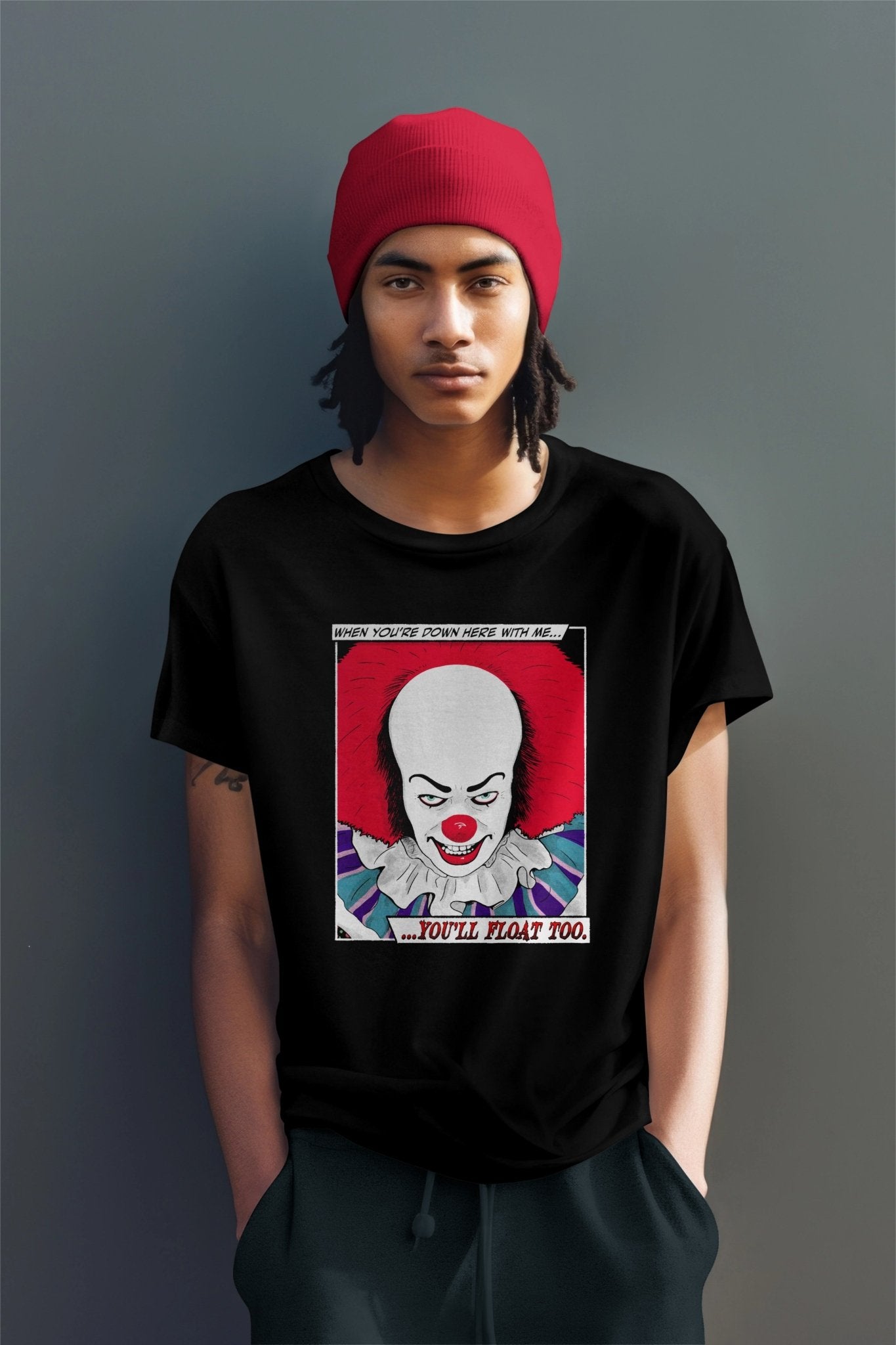 A man in a red cap wearing a You'll Float Too Pennywise Unisex Heavy Cotton Alternative Fashion T-Shirt by Glow Bat